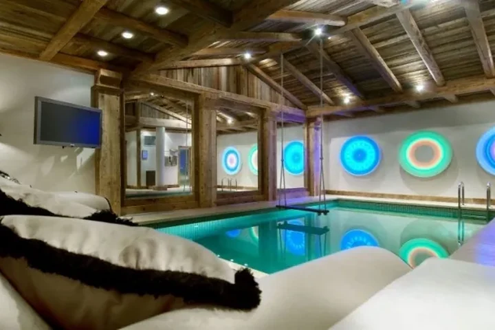 Chalet-Hallenbad mit Holzbalken und farbiger Wandbeleuchtung – Wellness im Skiurlaub
