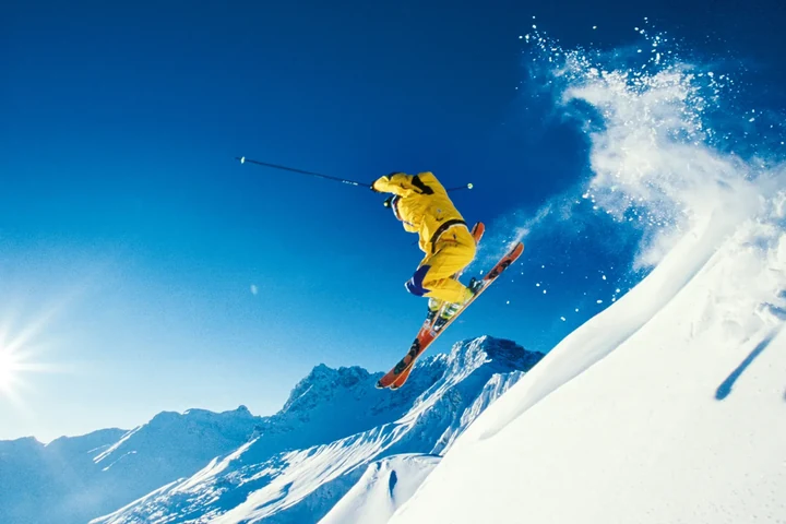 Skifahrer im gelben Anzug im Sprung über eine Schneekante vor Gipfeln und tiefblauem Himmel – Freeride und Skispaß