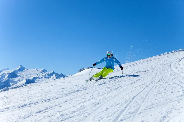 Skifahrerin in blauer Jacke beim Carven auf präparierter Piste unter wolkenlosem Himmel – Skifahren lernen und genießen