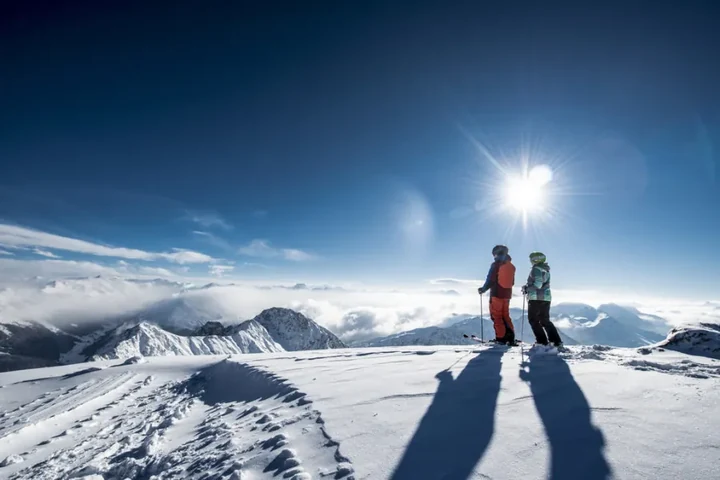 Zwei Skifahrer auf einem Gipfel im Gegenlicht über Wolken und Bergen – Skitour und Aussicht