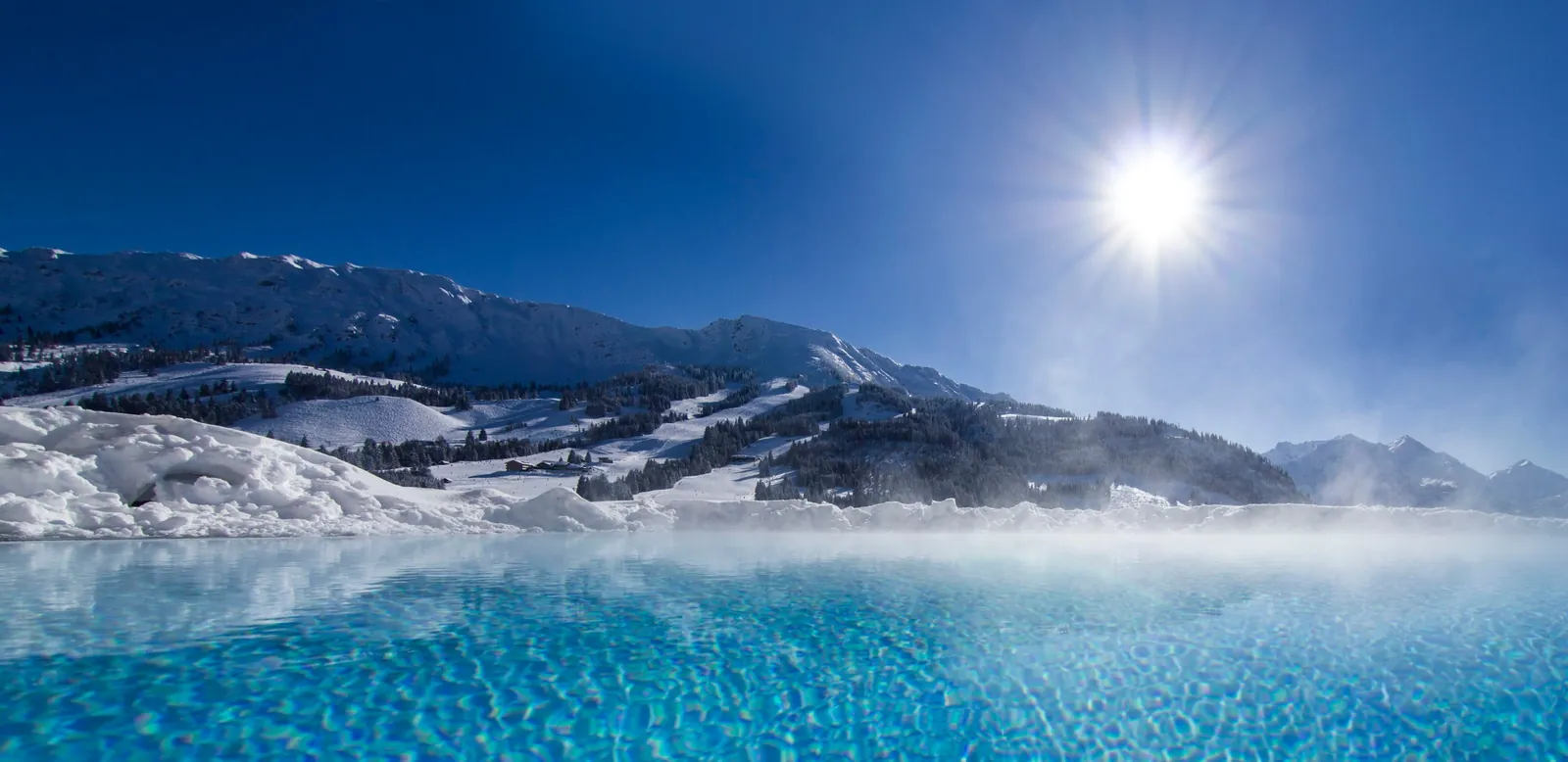Außenpool mit Bergblick Dampfender Außenpool mit Blick auf verschneite Berge und Sonne – Wellness im Skiurlaub